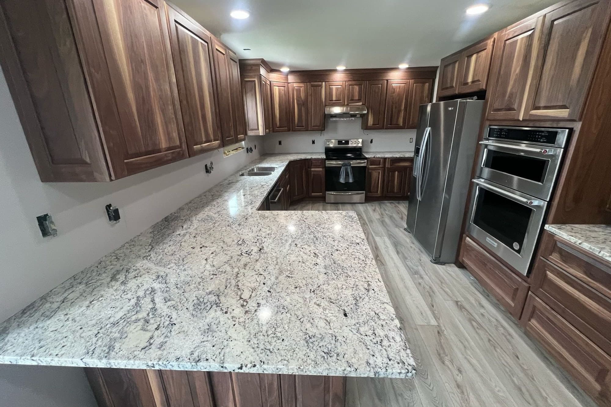 Cocina en U con cubiertas de granito blanco y gris moteado, península amplia, gabinetes en tono nogal y electrodomésticos de acero inoxidable