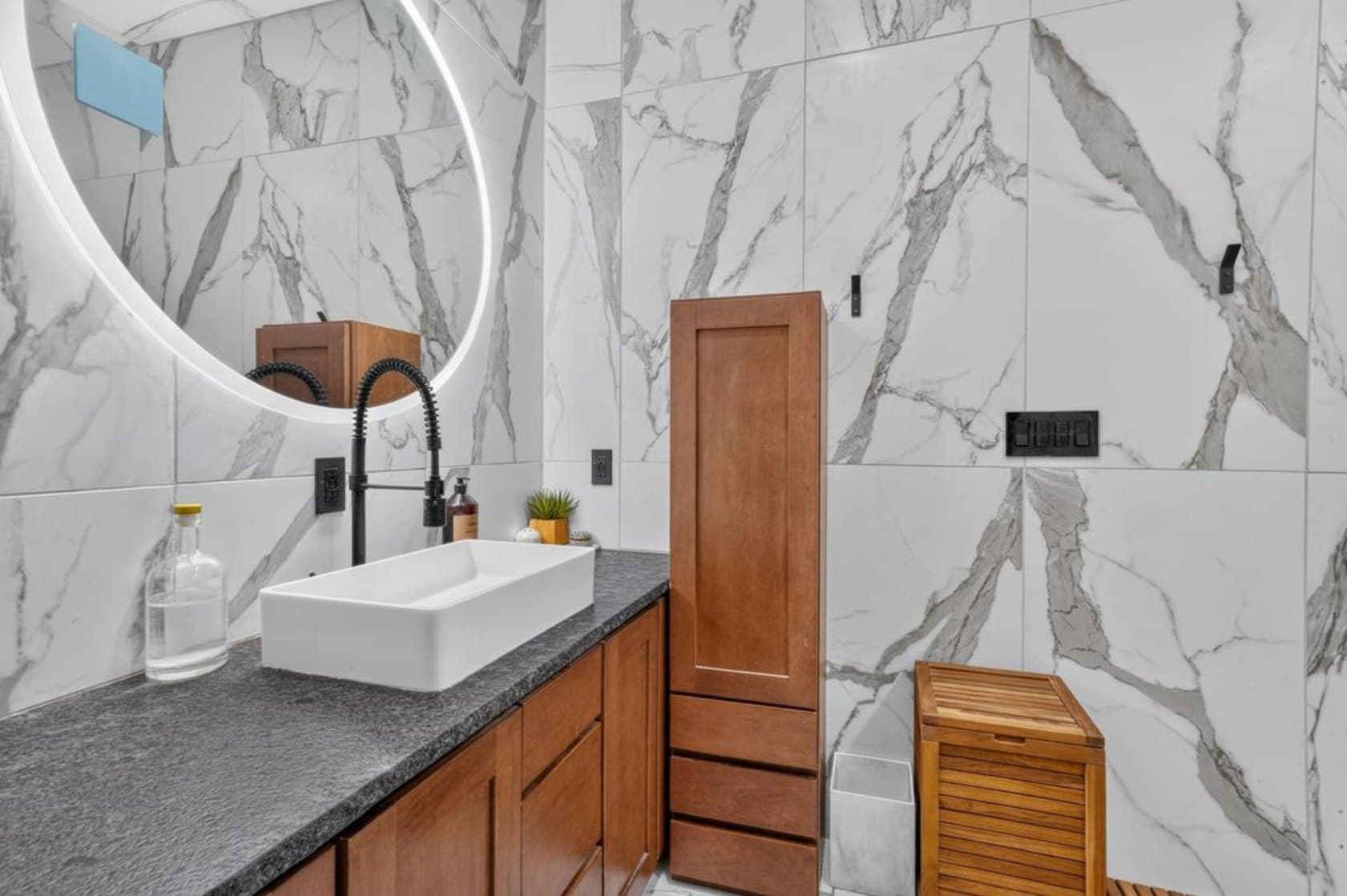 Baño a medida con grandes paneles de pared estilo mármol, mueble de madera con cubierta de piedra oscura, lavabo blanco sobre cubierta y grifería negra mate