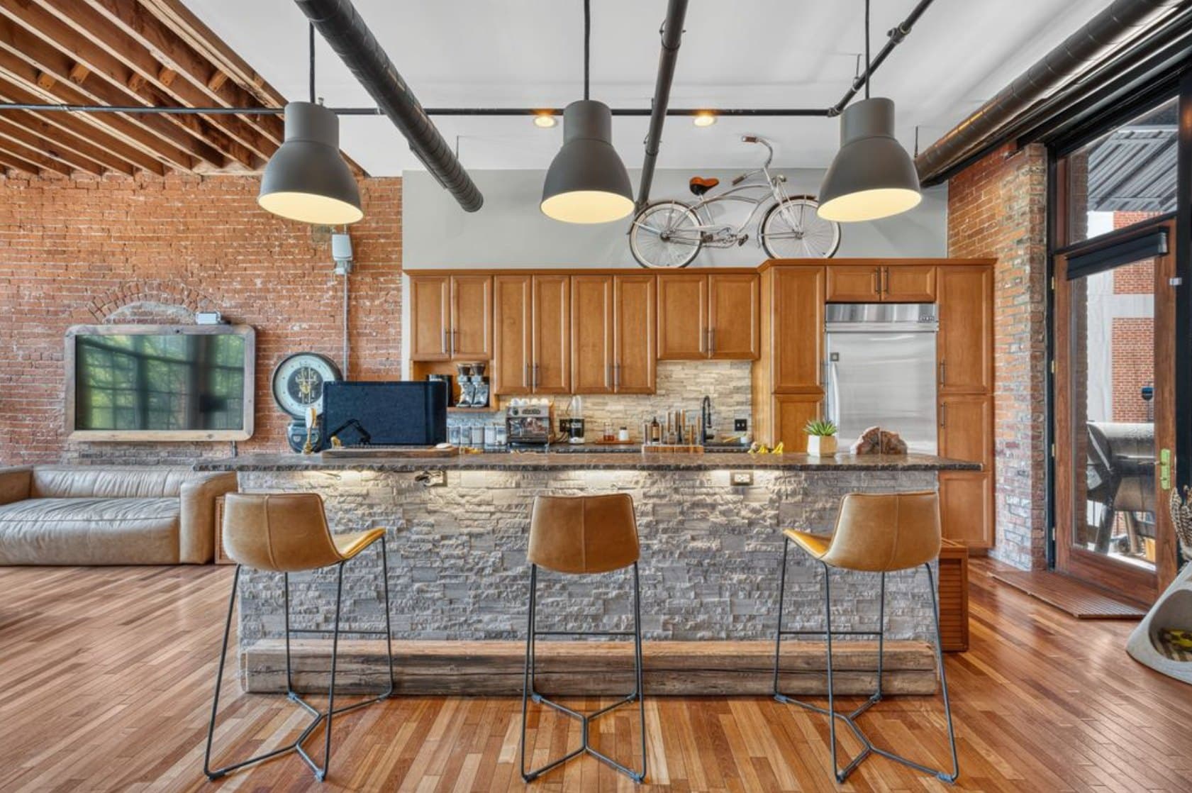 Isla de cocina en un loft revestida con muro de piedra apilada (ledger stone), cubierta de piedra oscura y bancos altos